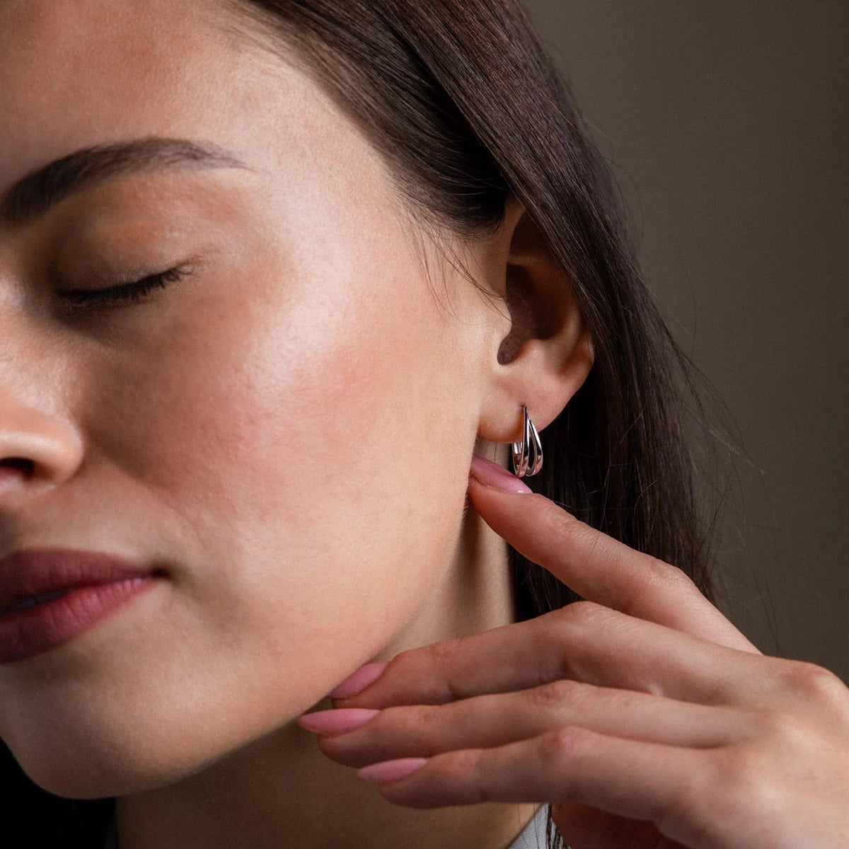 Close-up of a woman adjusting an earring with a neutral background