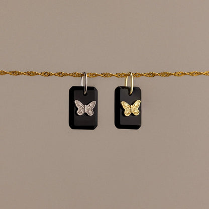 Butterfly-shaped earrings on a gold chain against a beige background