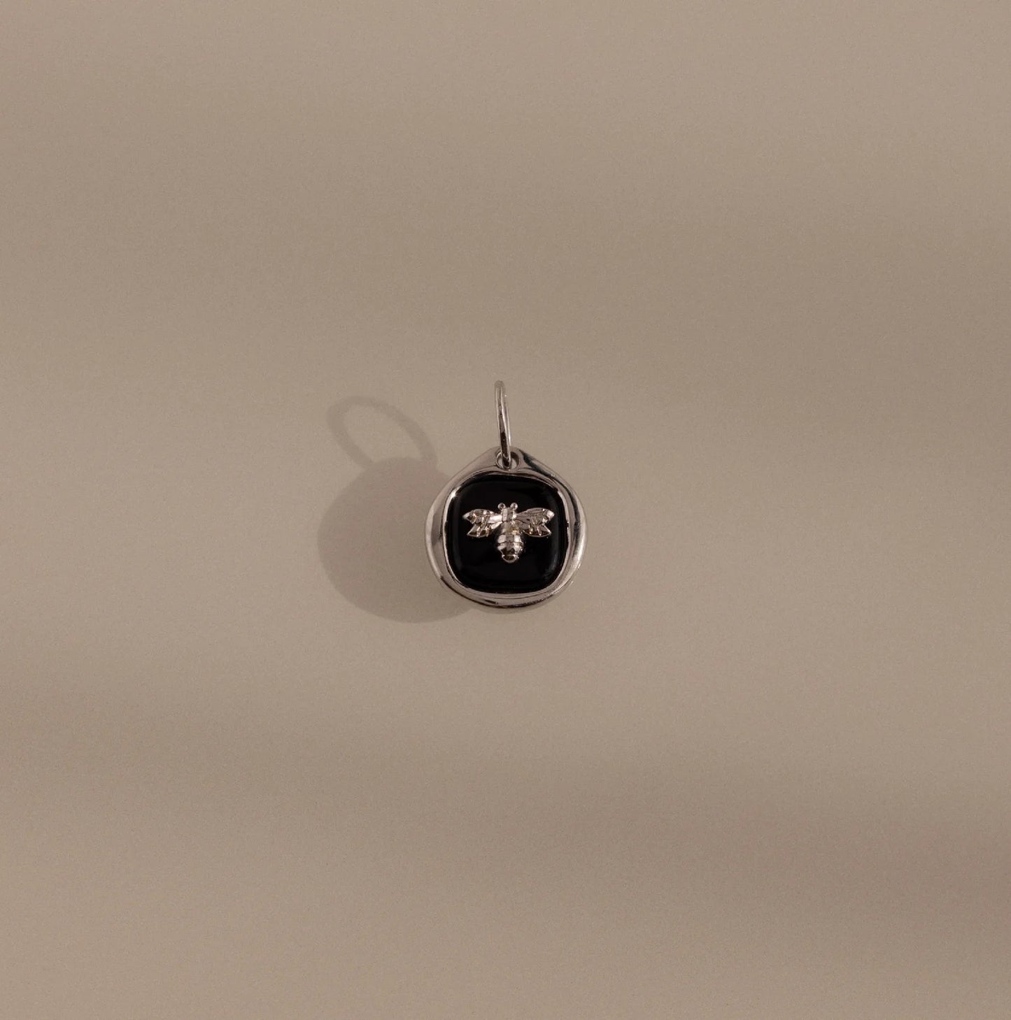 Silver pendant with a black circle and bee design on a beige background