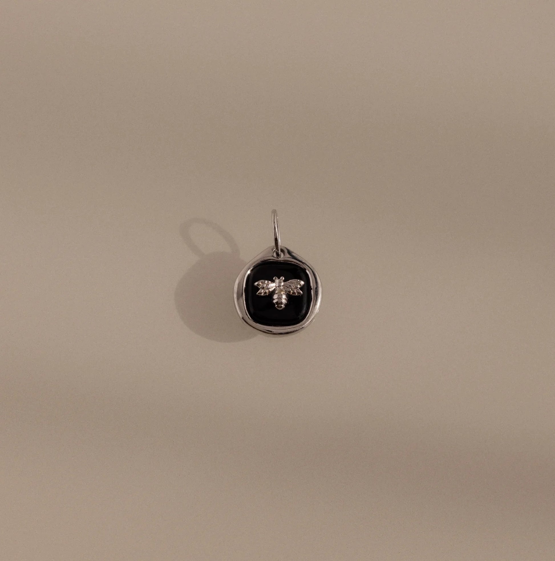 Silver pendant with a black circle and bee design on a beige background