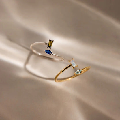 Two gold rings with gemstones on a beige fabric background