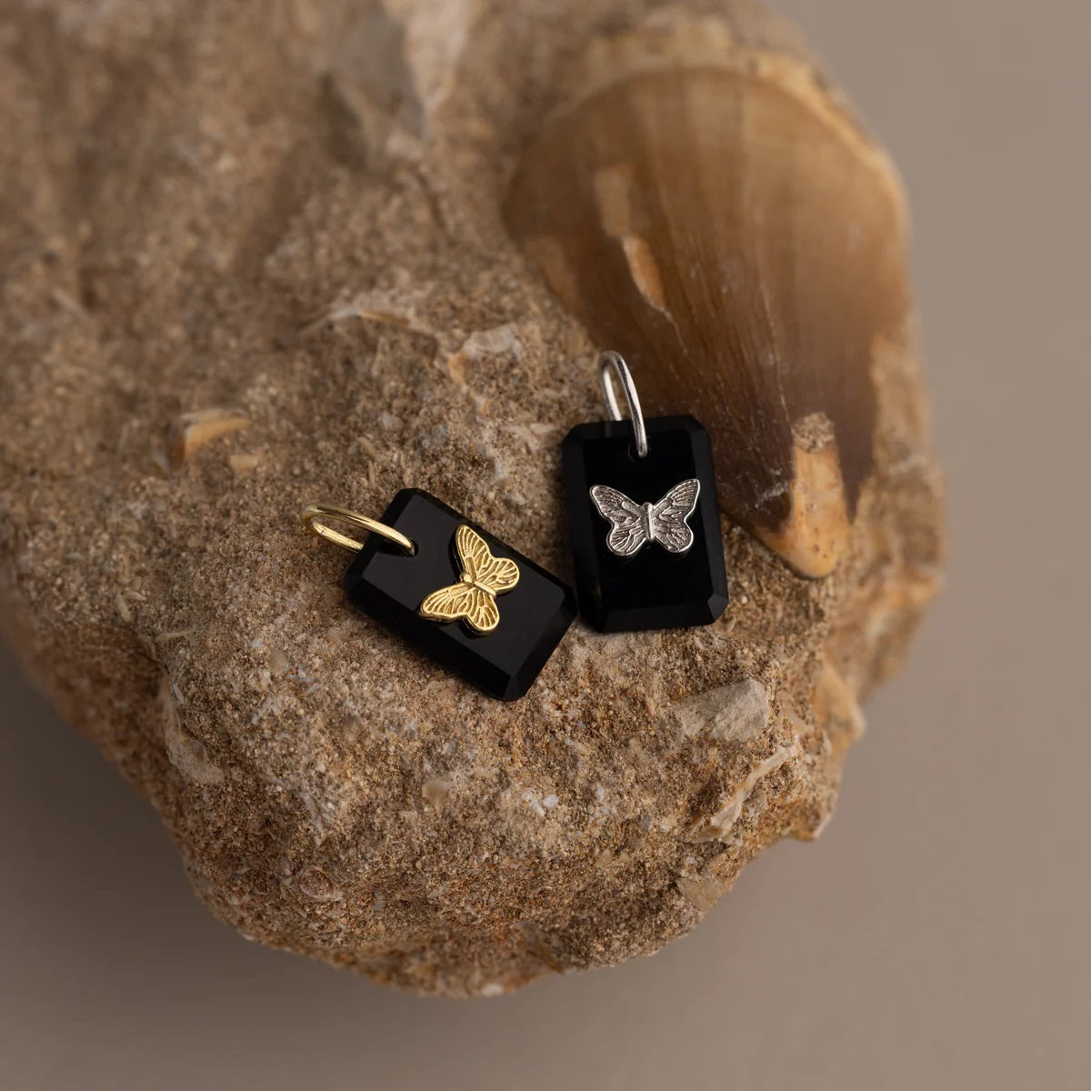 Two butterfly-shaped pendants on black stones with a natural stone background