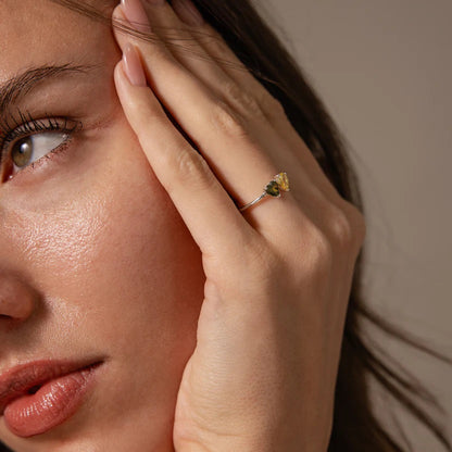 Close-up of a woman's face with a hand touching her cheek, wearing a ring with a yellow gemstone.