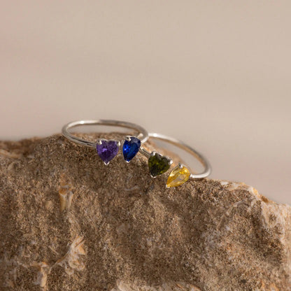 Silver ring with heart-shaped gemstones on a stone surface