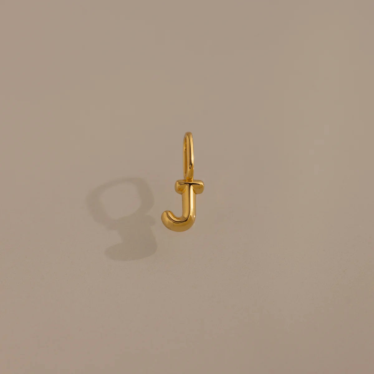 Gold letter 'J' charm on a beige background