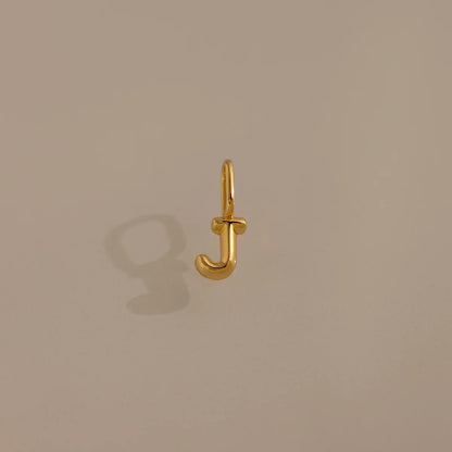 Gold letter 'J' charm on a beige background