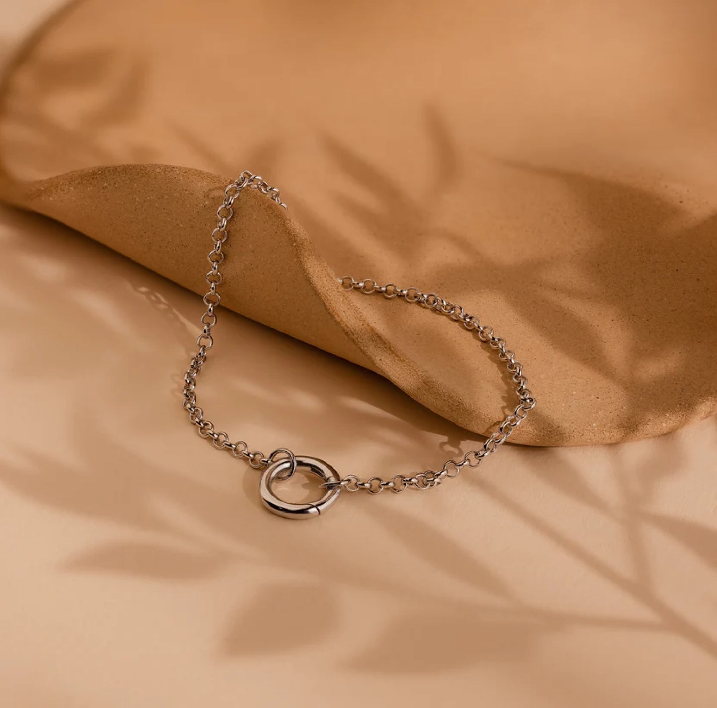Silver chain bracelet with a heart clasp on a beige fabric background
