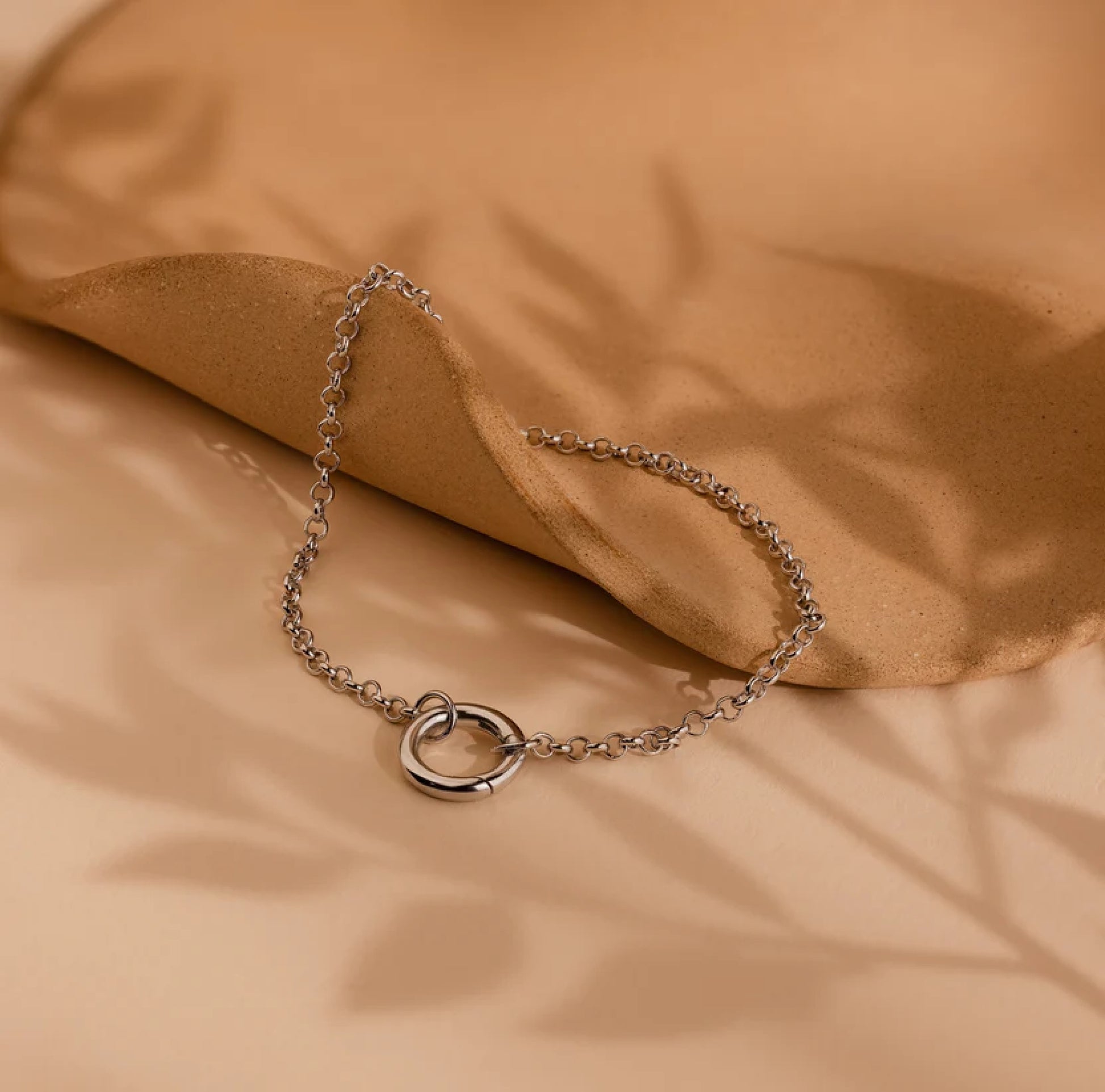 Silver chain bracelet with a heart clasp on a beige fabric background