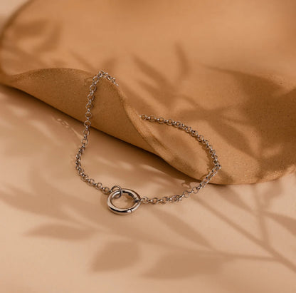 Silver chain bracelet with a heart clasp on a beige fabric background