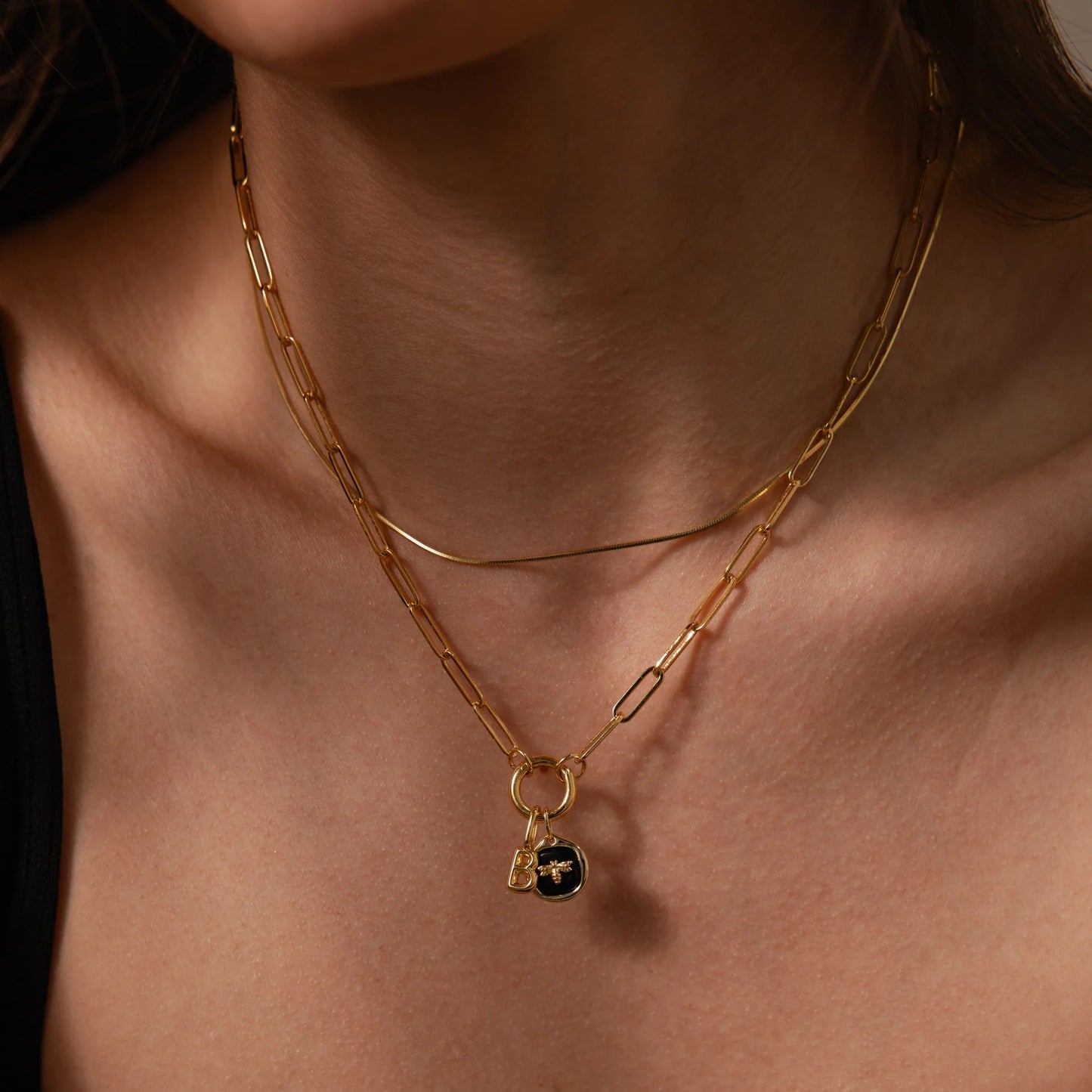 Close-up of a person wearing a gold chain necklace with a pendant on a neutral background