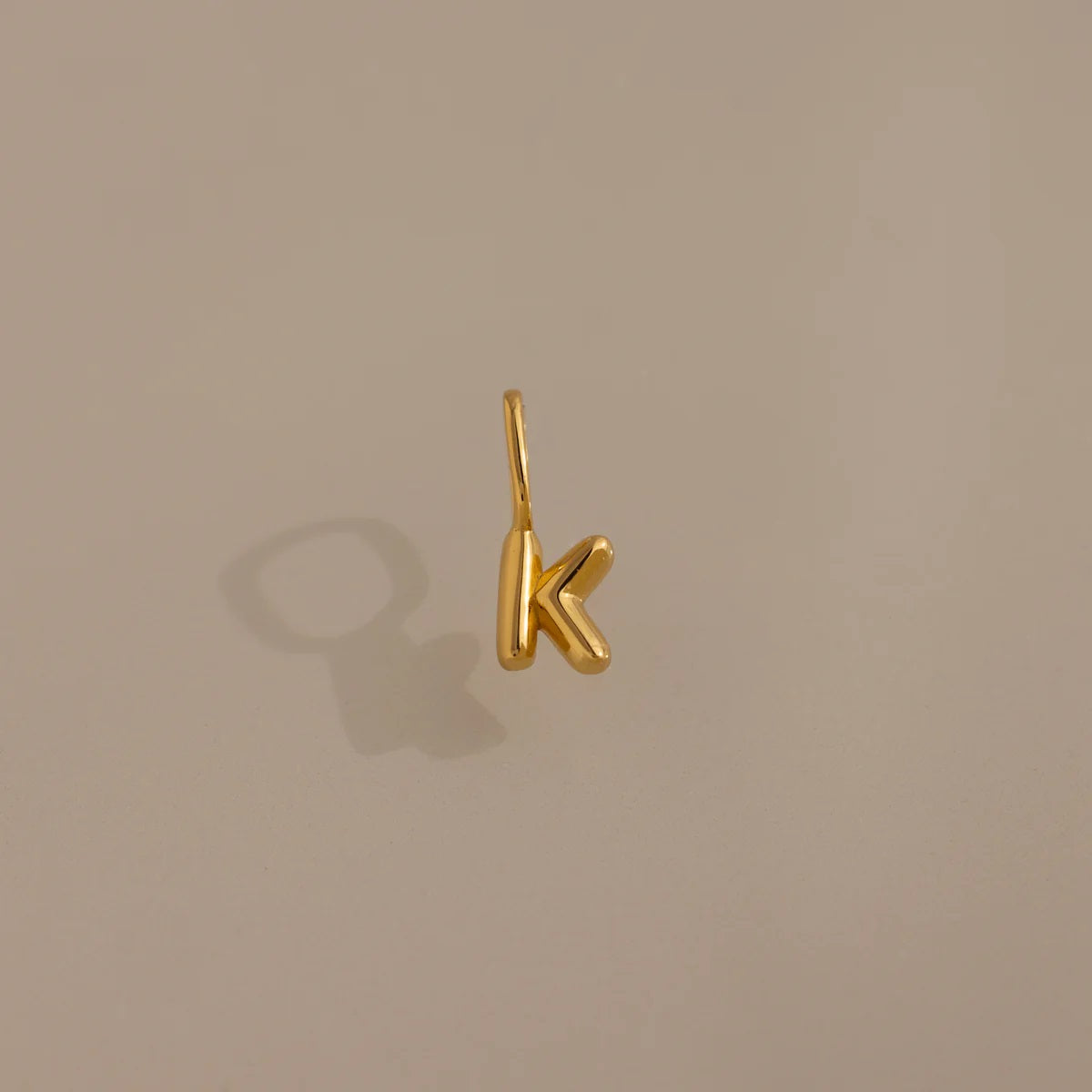 Gold letter 'K' pendant on a beige background