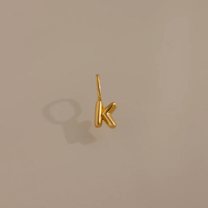 Gold letter 'K' pendant on a beige background