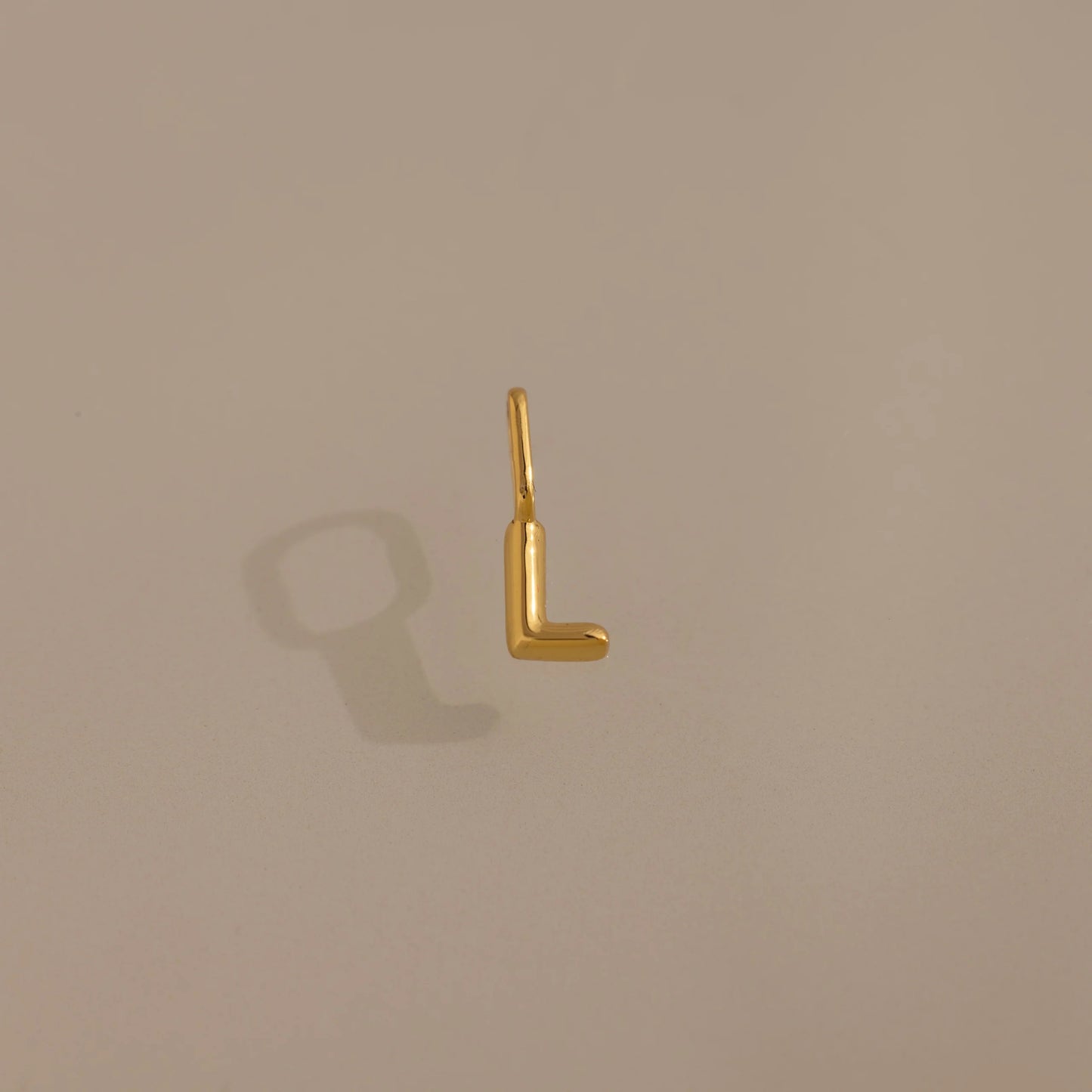 Gold letter 'L' charm on a beige background