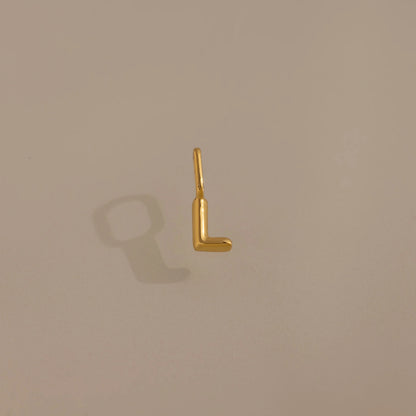 Gold letter 'L' charm on a beige background