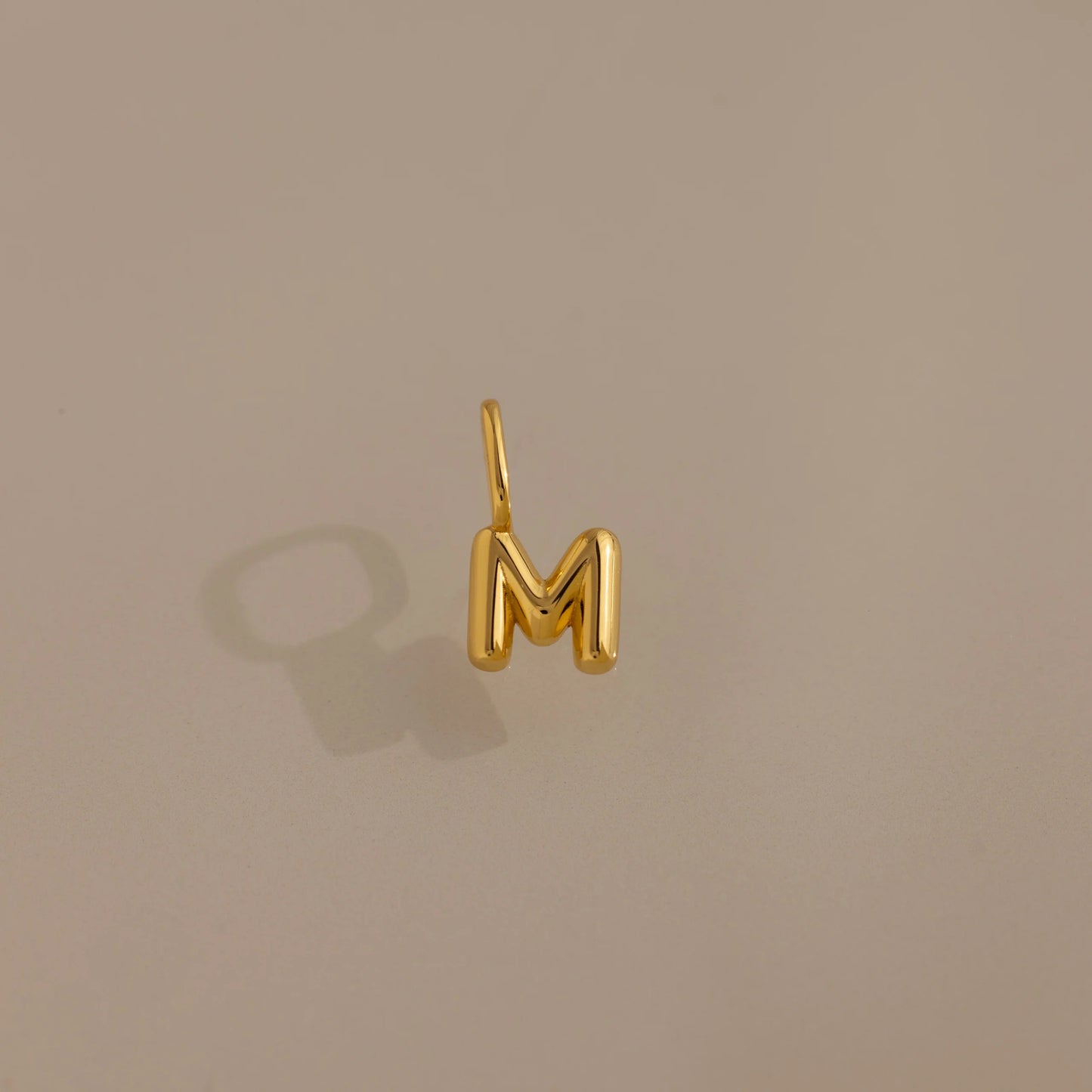 Gold letter 'M' charm on a beige background
