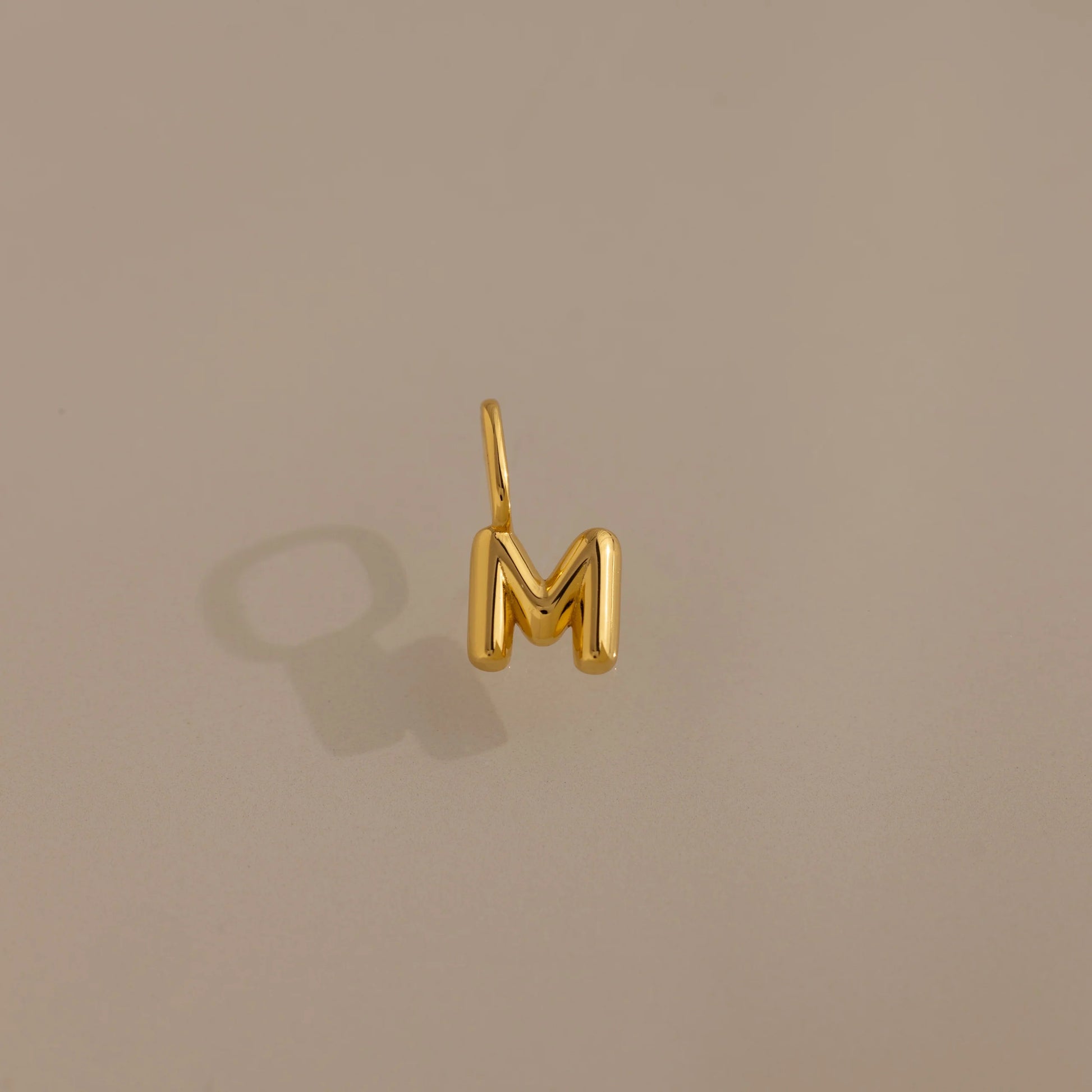Gold letter 'M' charm on a beige background