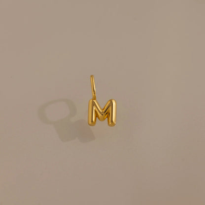 Gold letter 'M' charm on a beige background