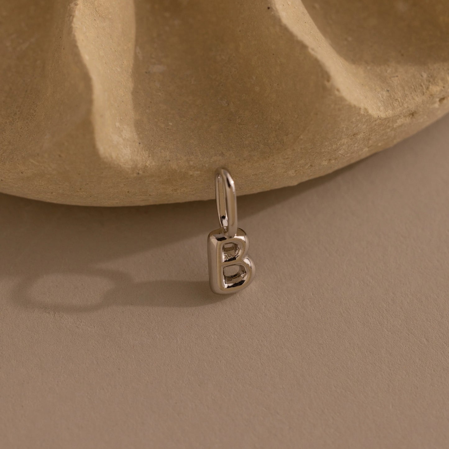 Silver 'B' pendant on a beige stone background