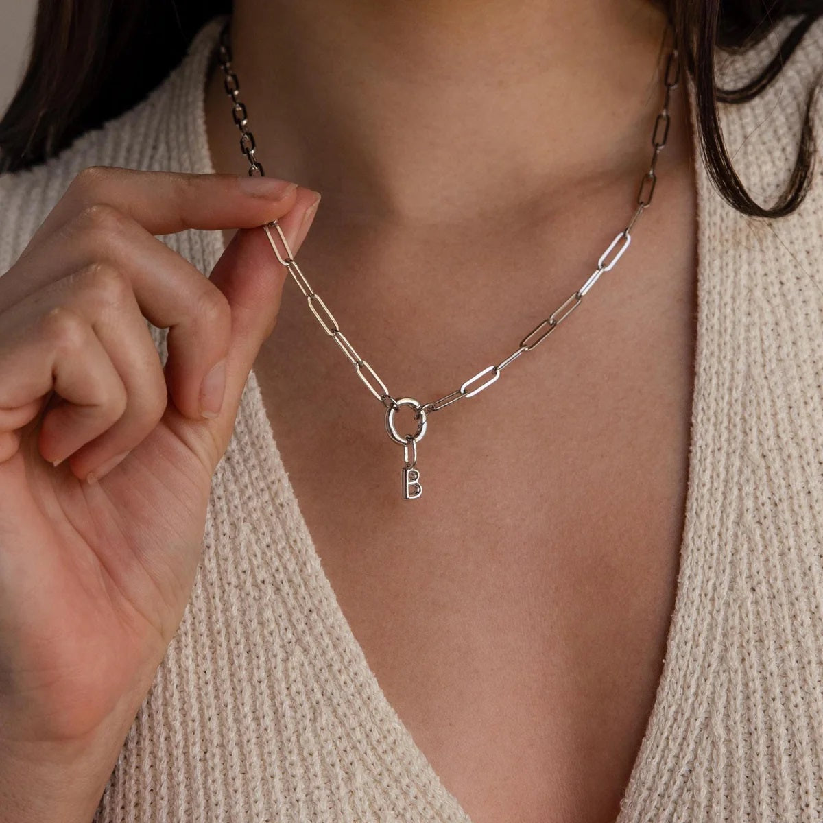 Necklace with a letter 'B' charm being adjusted by a hand against a neutral background