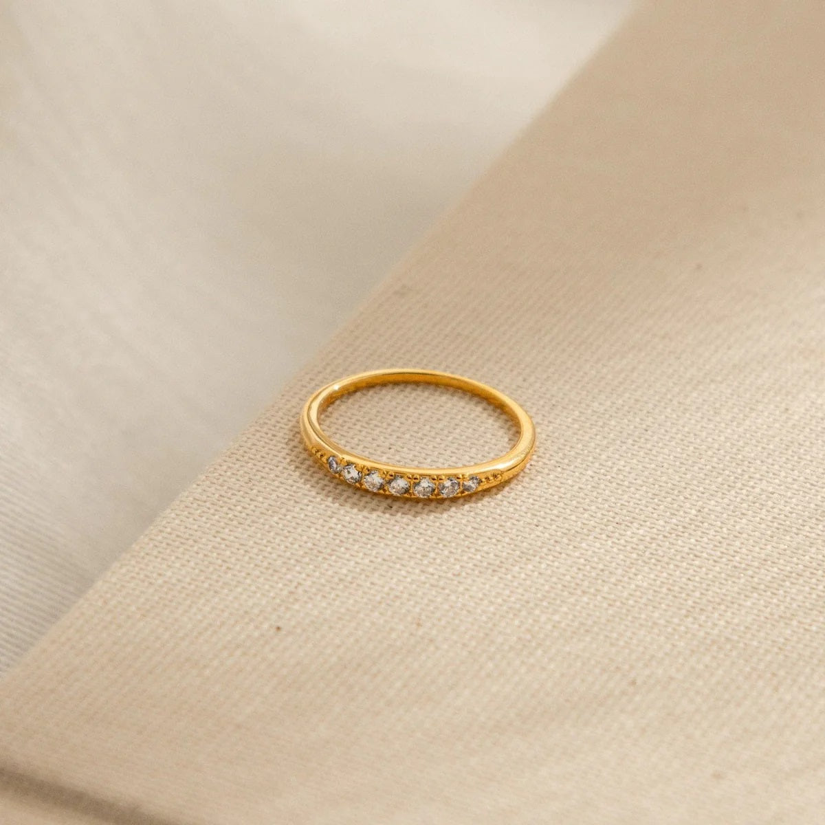 Gold ring with small diamonds on a beige fabric background