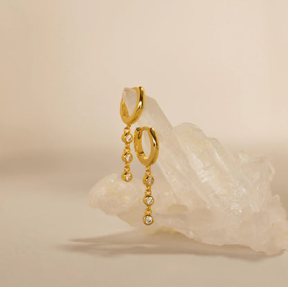 Gold hoop earrings with chain and gemstone drop on a beige background