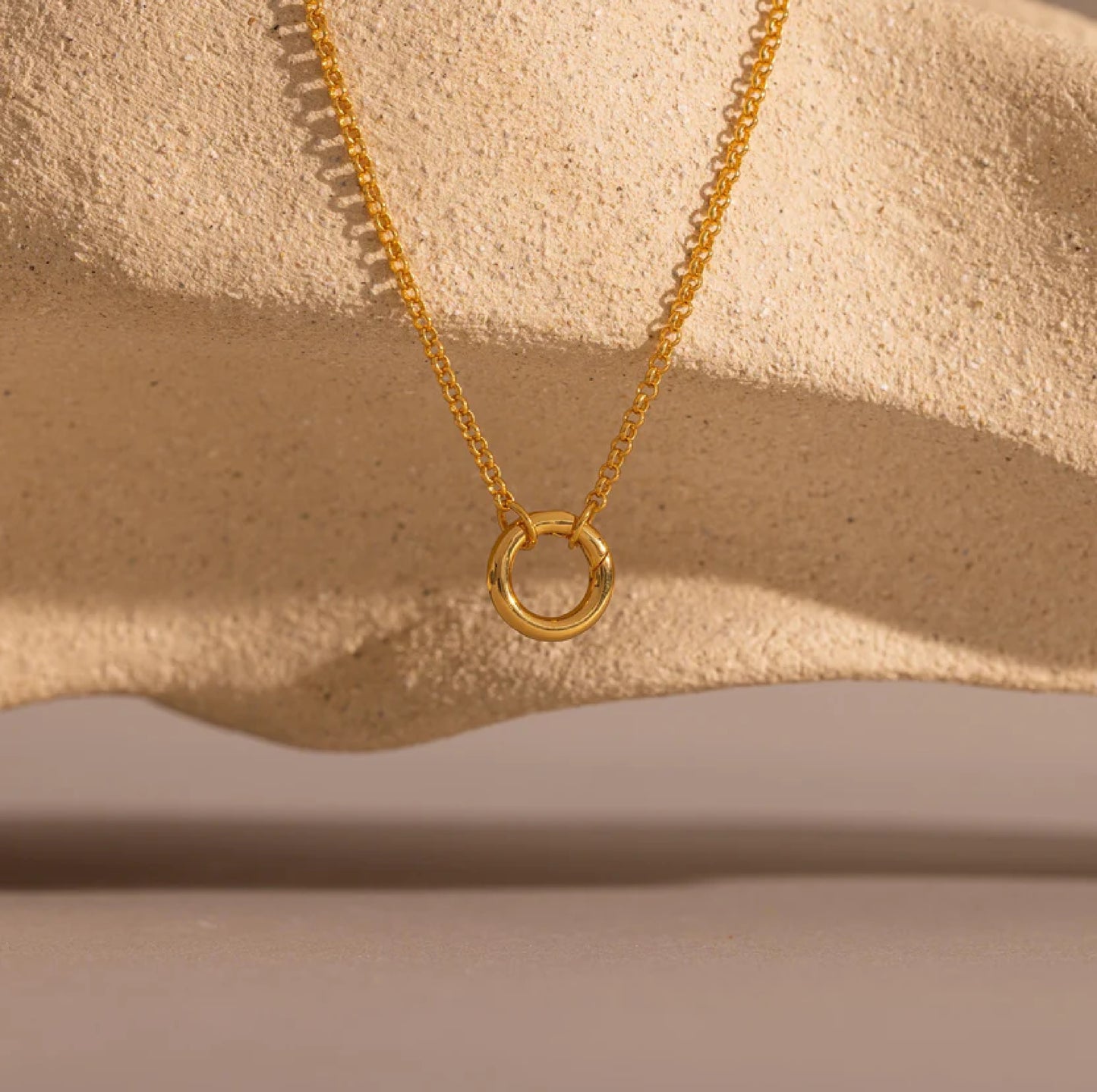 Gold necklace with a circular pendant on a beige background