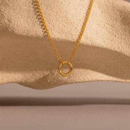 Gold necklace with a circular pendant on a beige background