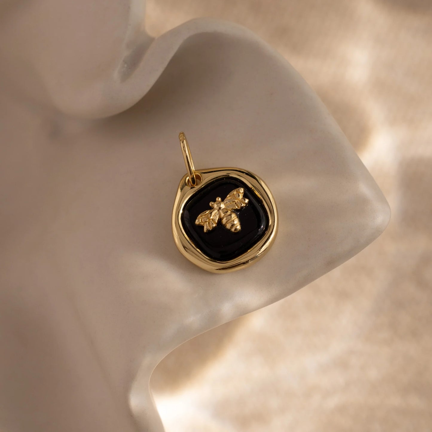 Gold pendant with a black stone and bee design on a soft beige background