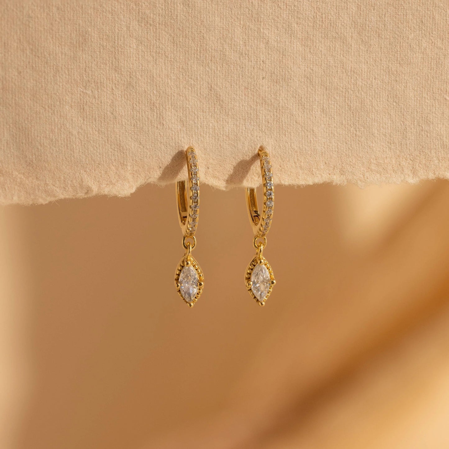 Gold earrings with clear stones on a beige background