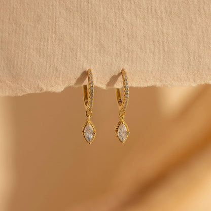 Gold earrings with clear stones on a beige background