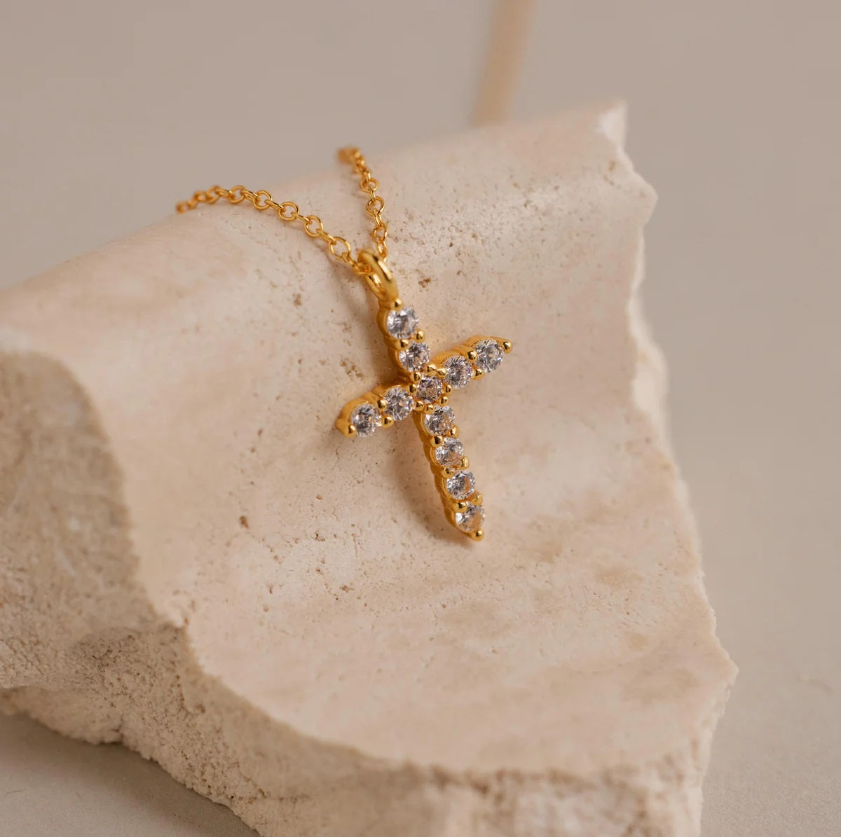 Gold necklace with a star-shaped pendant on a beige stone background