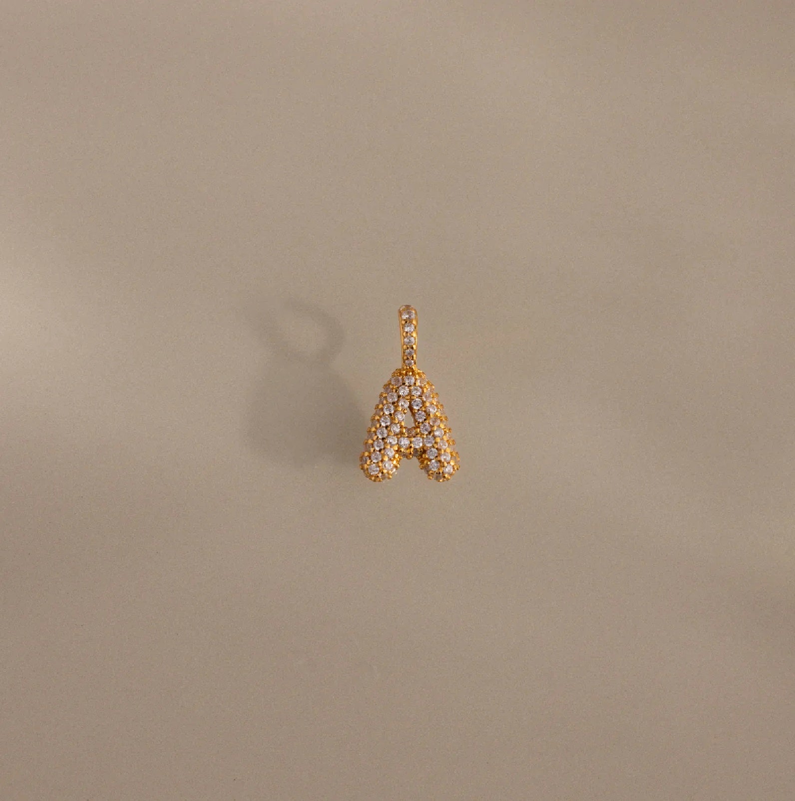 Gold letter 'A' pendant with diamonds on a beige background