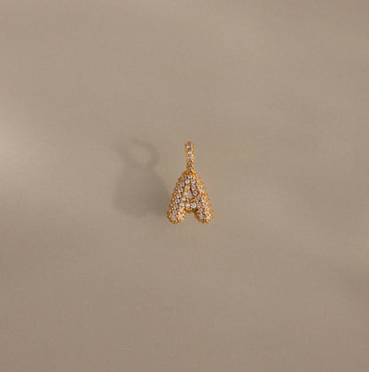 Gold letter 'A' pendant with diamonds on a beige background