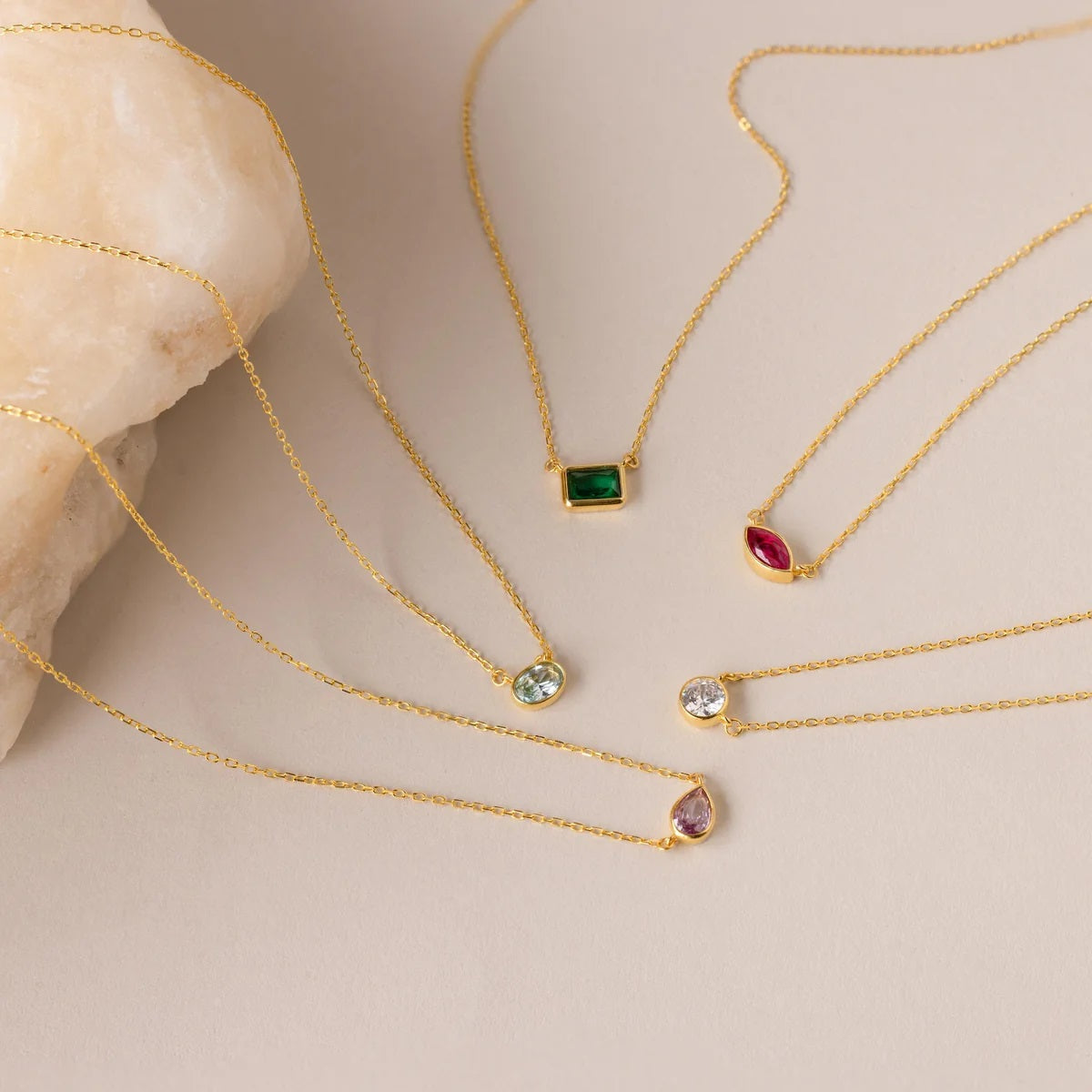 Gold necklaces with gemstone pendants on a beige surface