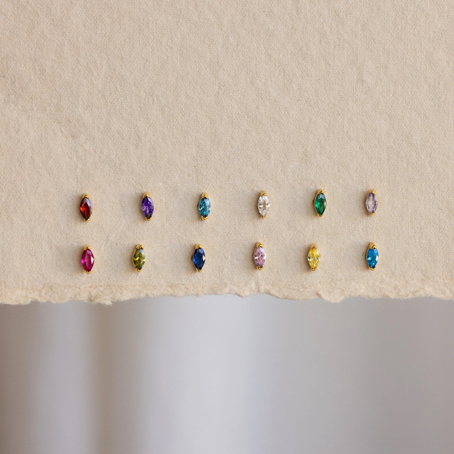 Row of multicolored gemstone earrings on a beige background