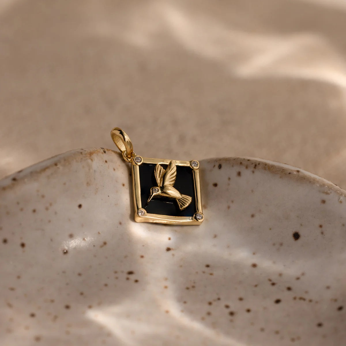 Gold pendant with a black square design on a ceramic dish