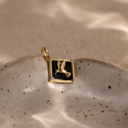 Gold pendant with a black square design on a ceramic dish