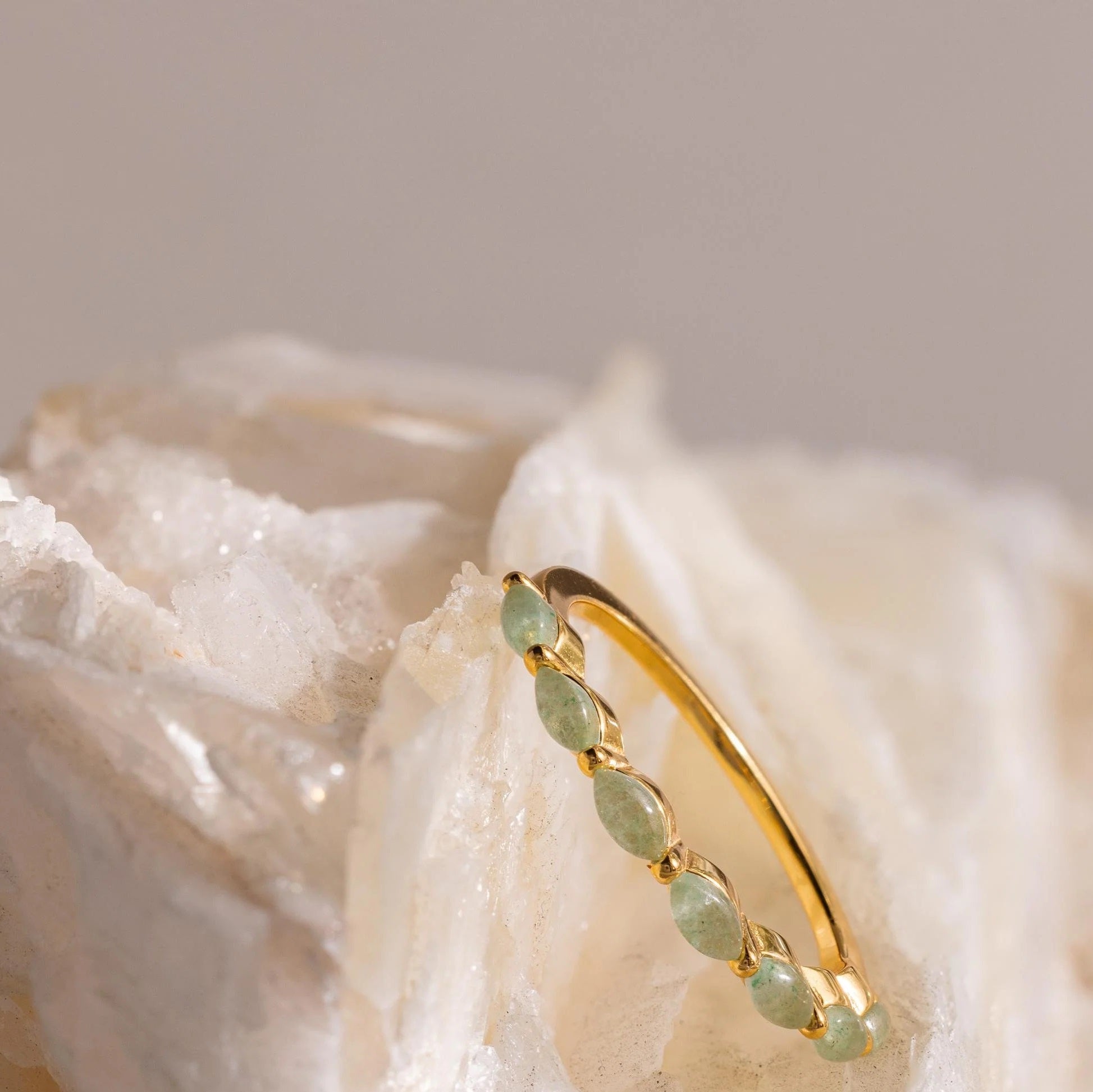 Gold hoop earring with green gemstones on a textured beige background