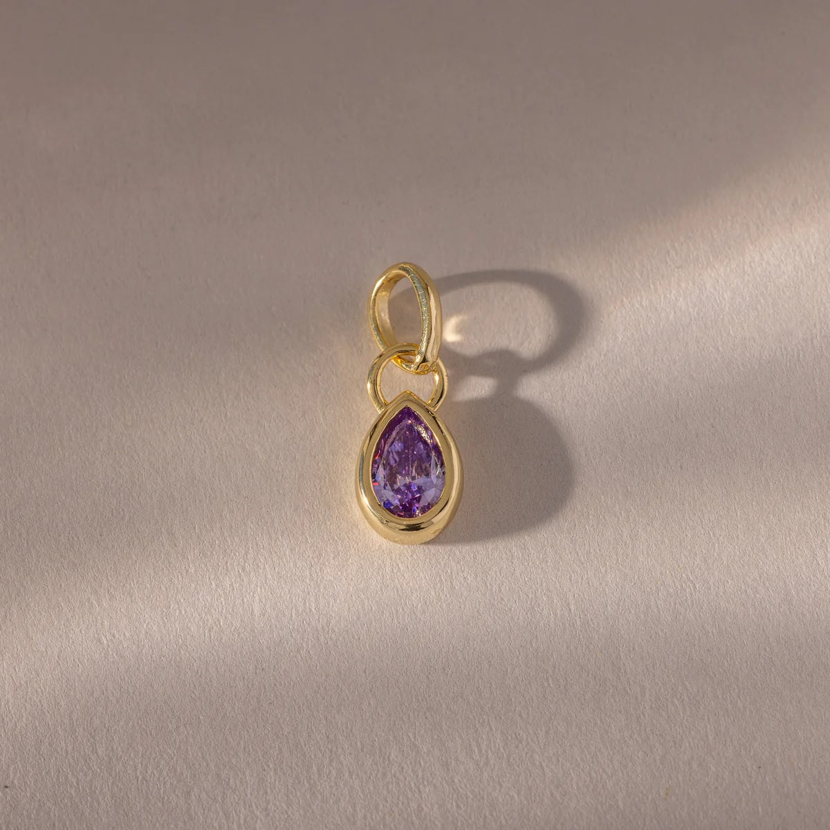 Gold pendant with a purple teardrop-shaped gemstone on a gray background