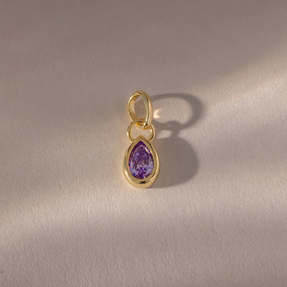 Gold pendant with a purple teardrop-shaped gemstone on a gray background