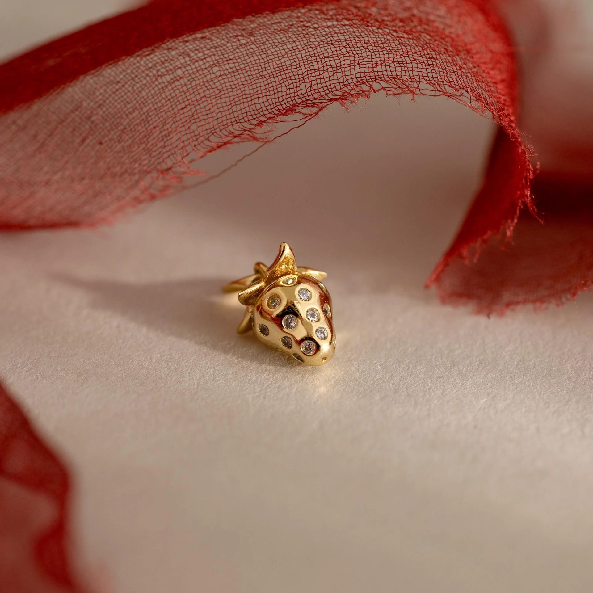 Gold strawberry-shaped jewelry piece with embedded stones on a soft fabric background