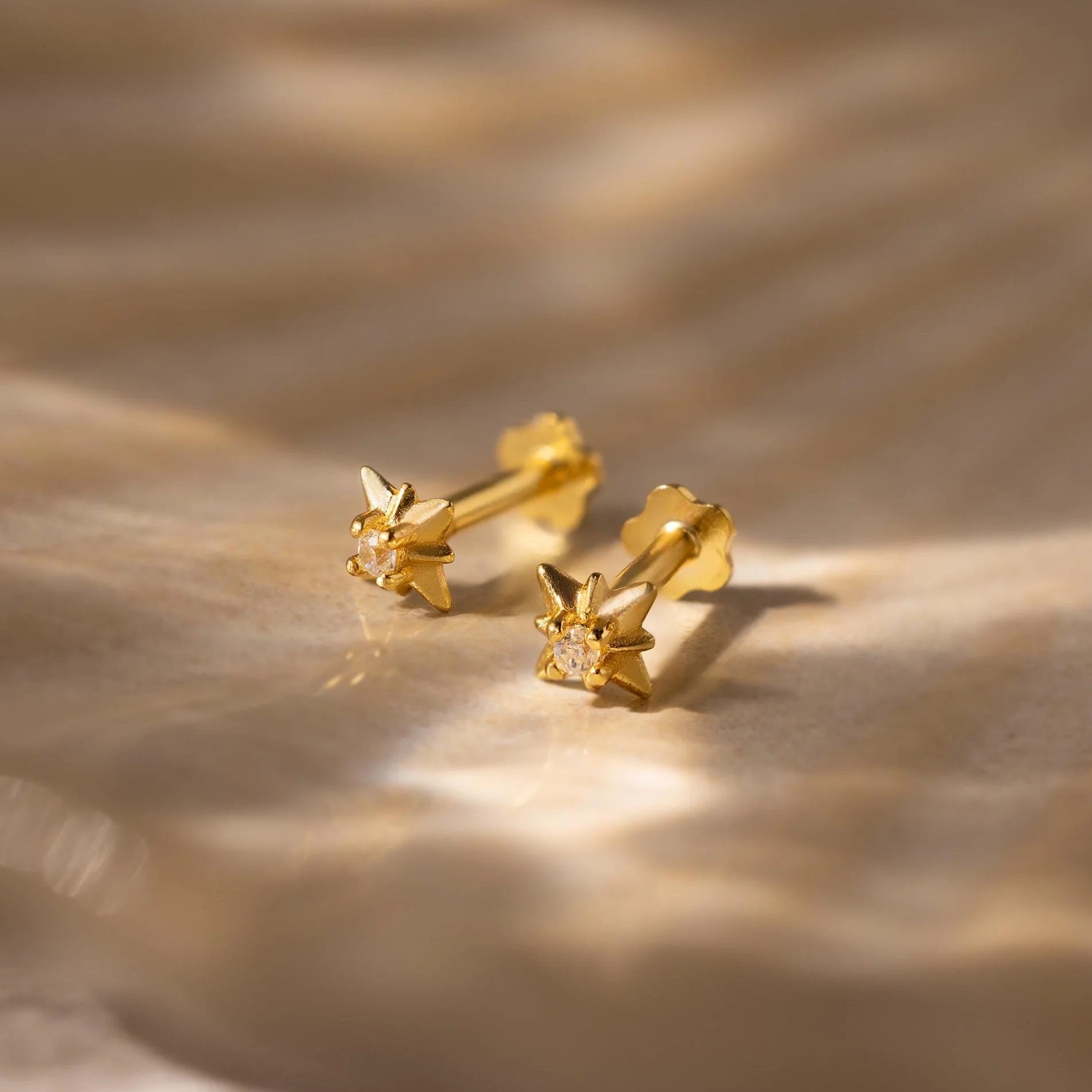 Gold earrings with a diamond on a textured beige surface
