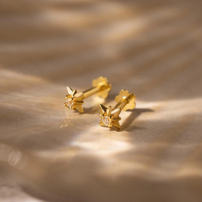 Gold earrings with a diamond on a textured beige surface