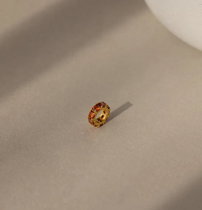 Gold ring with embedded stones on a beige surface