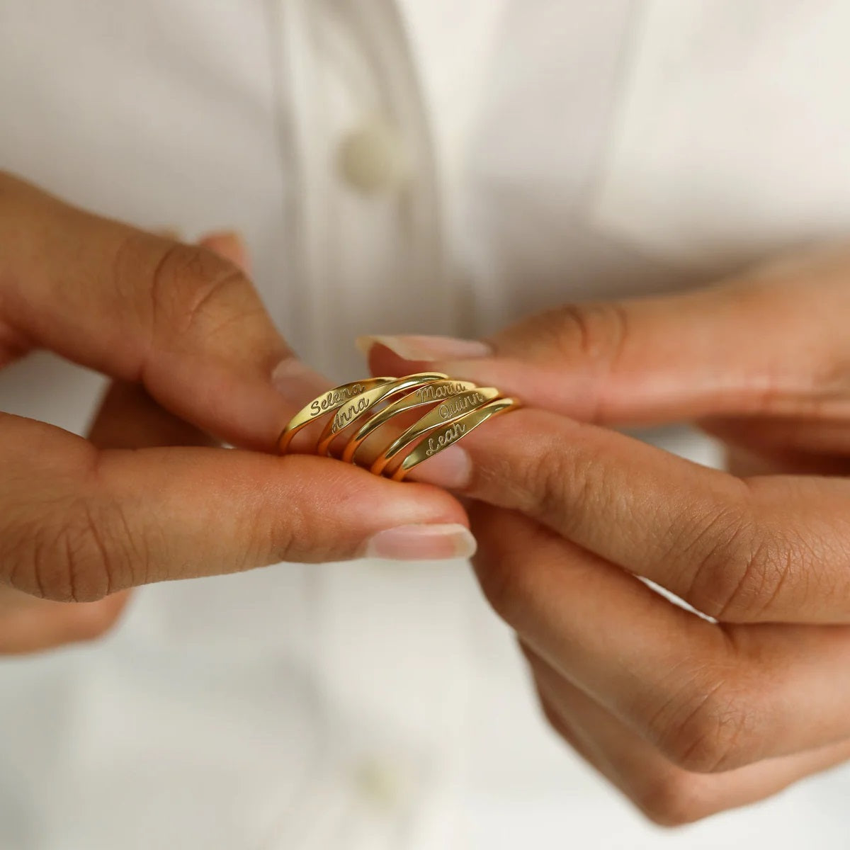 Gold ring with engraved text held between two hands against a white background