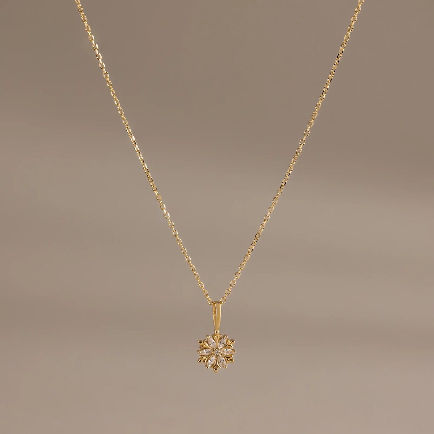 Gold necklace with a floral pendant on a brown background