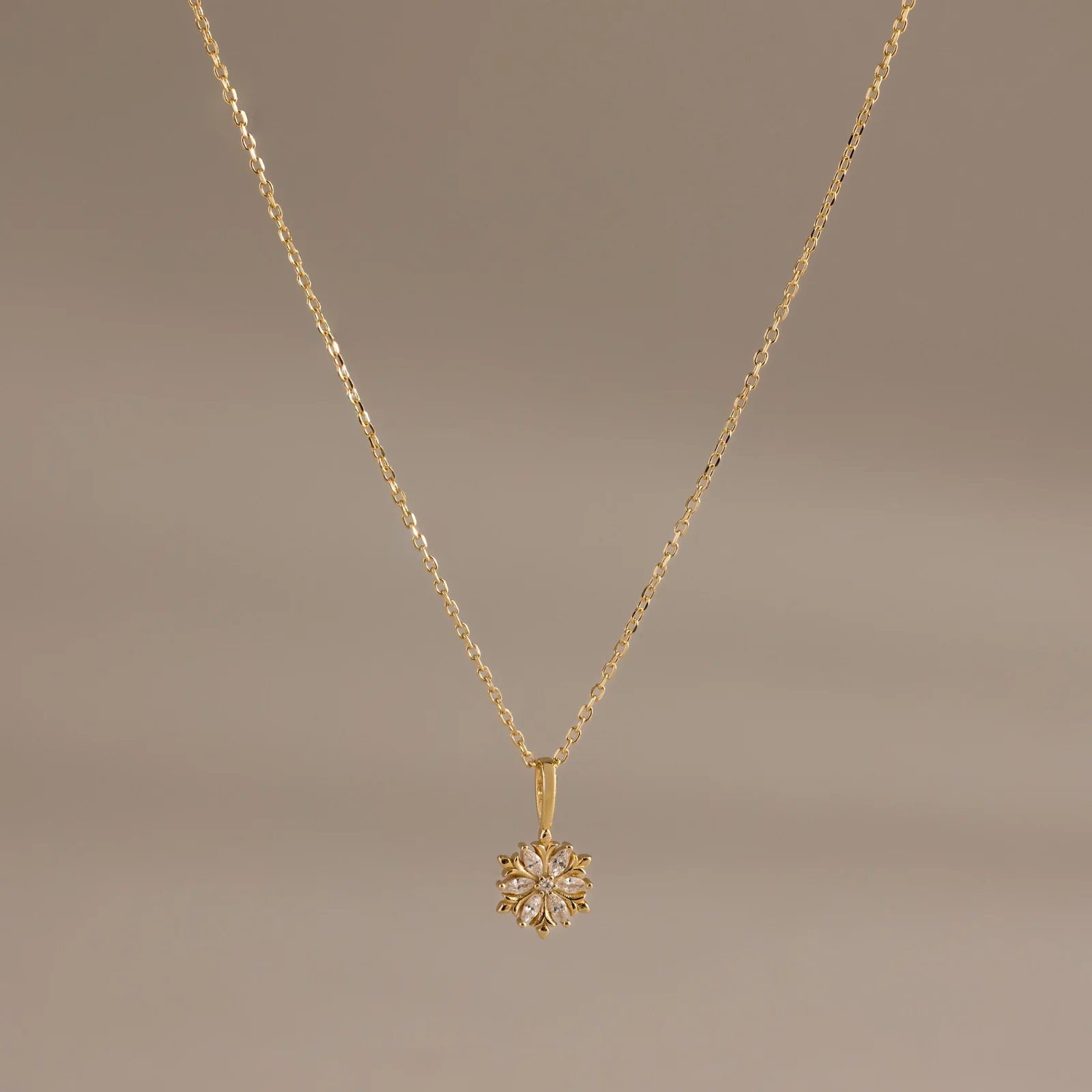 Gold necklace with a floral pendant on a brown background