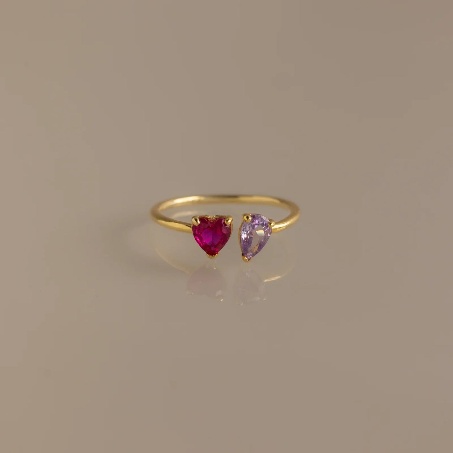 Gold ring with heart-shaped ruby and amethyst stones on a beige background