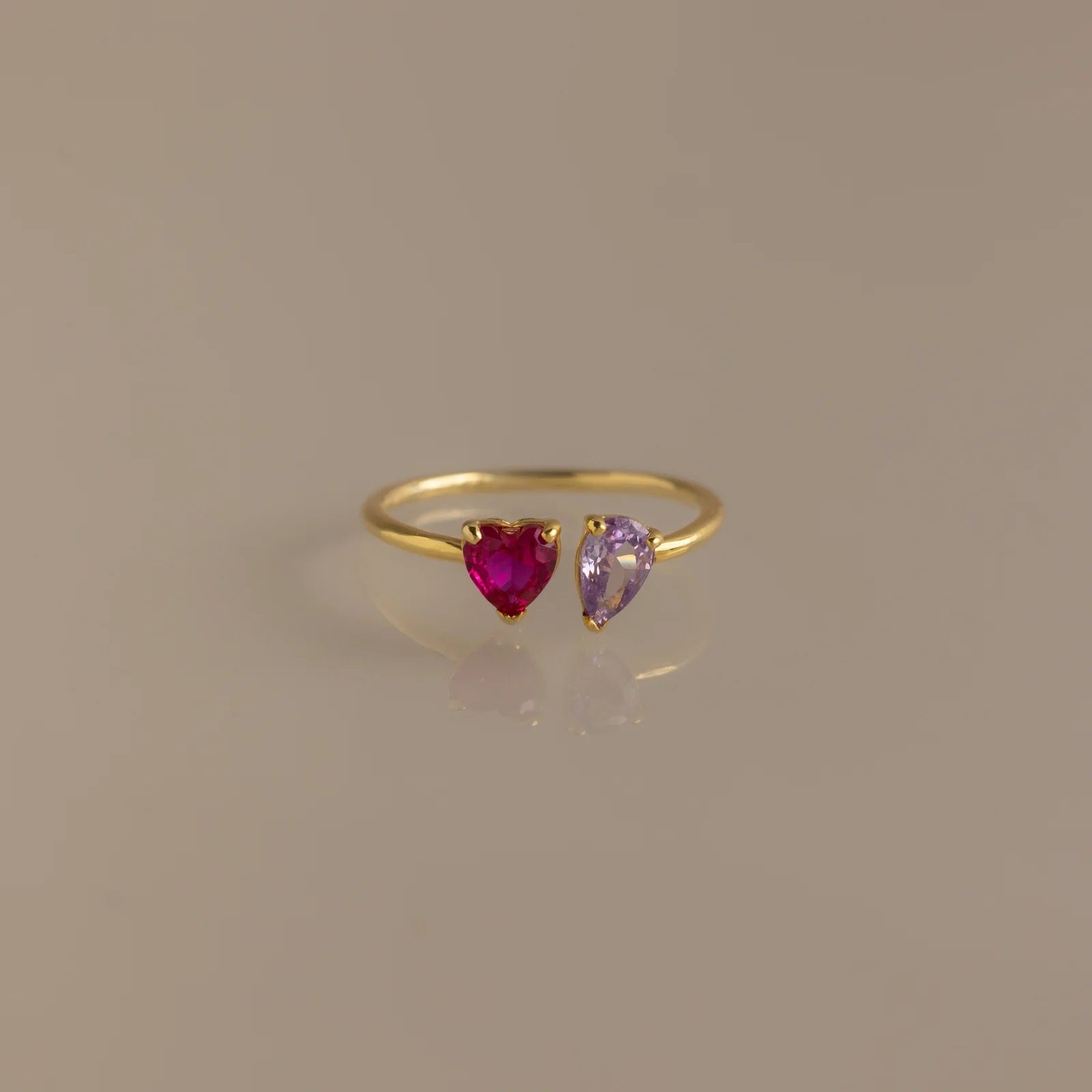 Gold ring with heart-shaped ruby and amethyst stones on a beige background