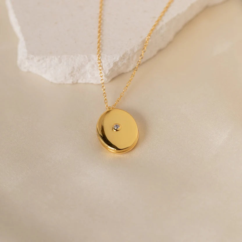 Gold necklace with a round pendant on a beige surface